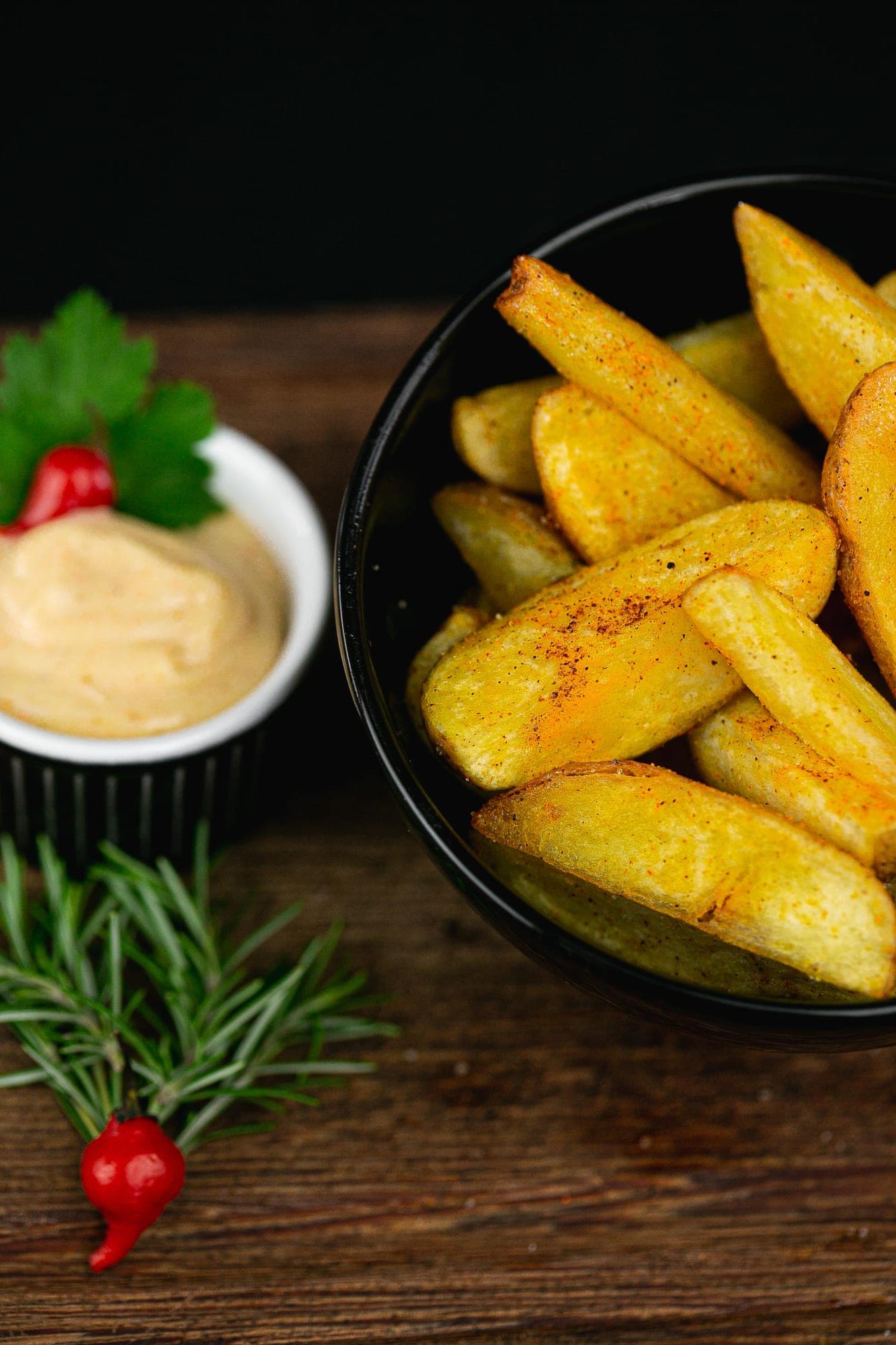 Batatas rústicas temperadas em tigela preta com molho cremoso, alecrim e pimenta