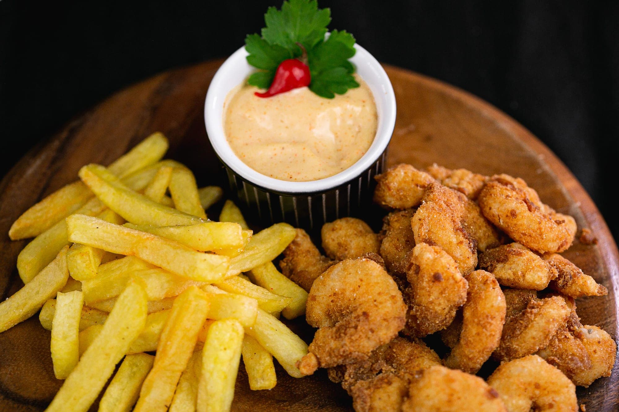 Iscas de camarão empanado e batatas fritas com molho cremoso picante em tábua de madeira